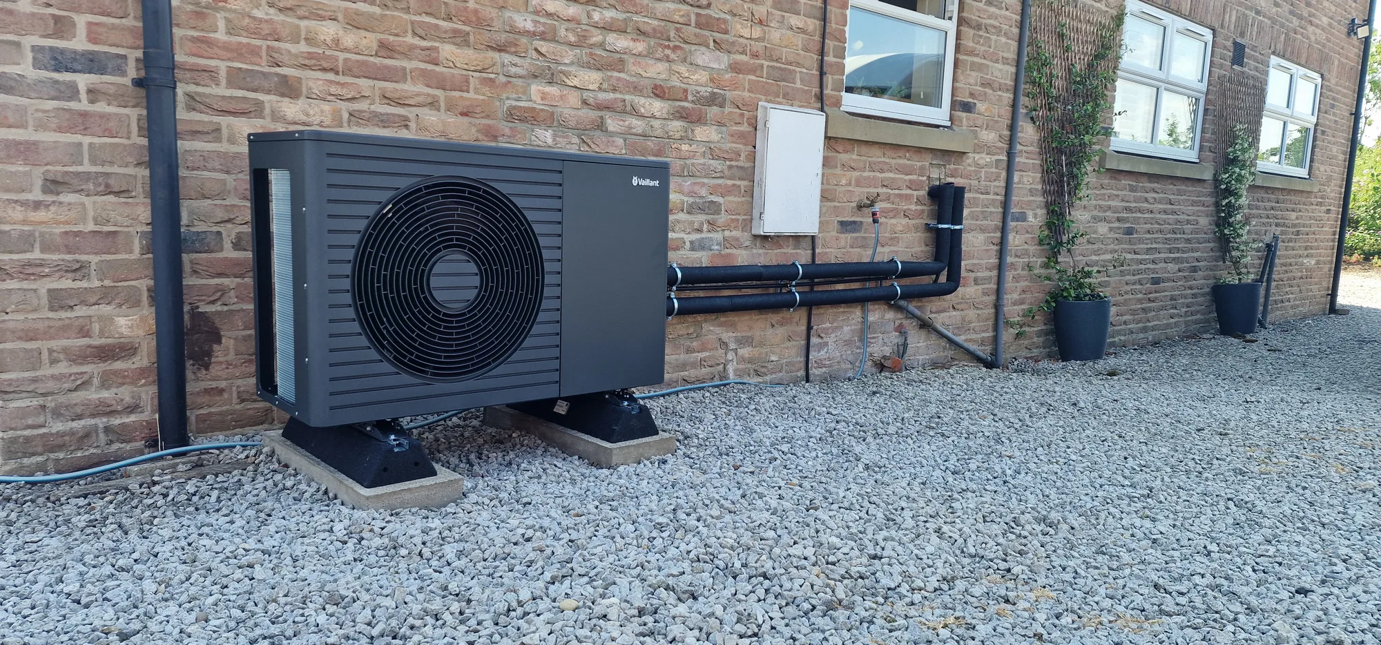 Vaillant air-source heat pump installation by PCR Plumbers near York and Selby New Vaillant air-source heat pump installed outside a rural brick home by PCR Plumbers, with insulated pipework and a raised gravel base